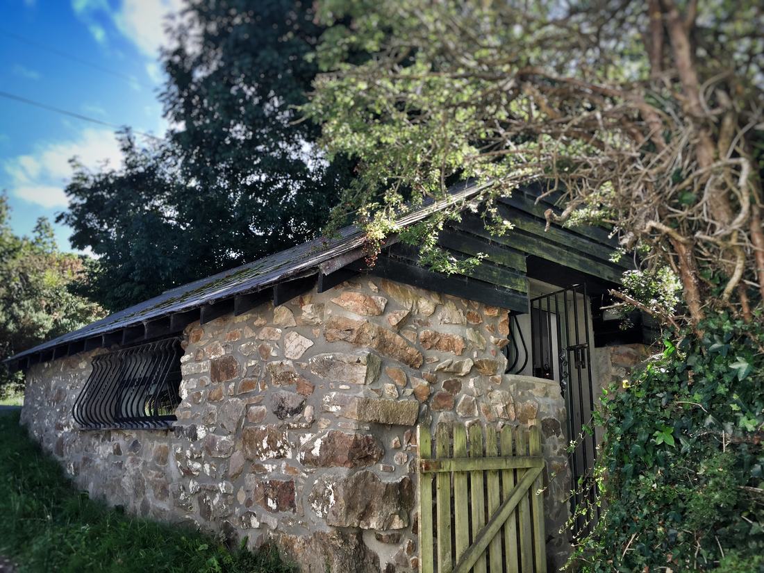The converted stone cowshed that houses the edit suite, under trees with a wooden gate