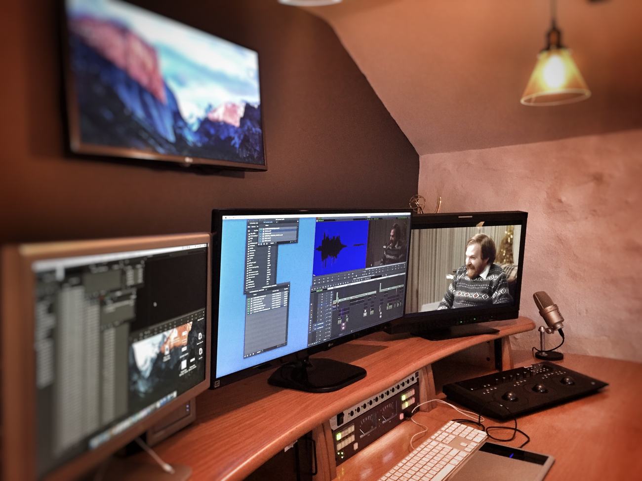 The editing desk: three monitors showing a timeline and a scene, with a grading control surface and microphone